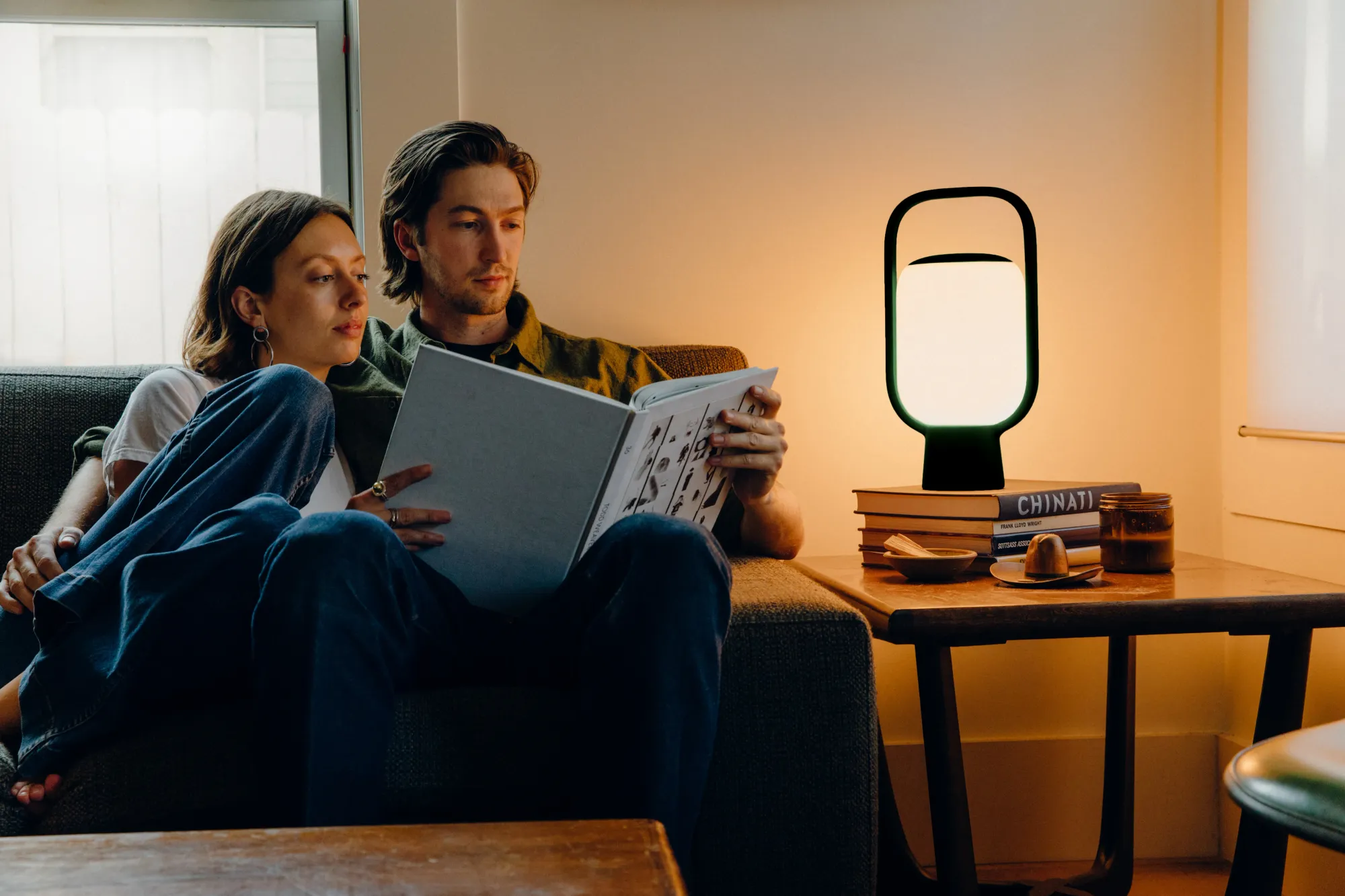 A couple reads a book together in their living room, illuminated by a black Kero Table Light