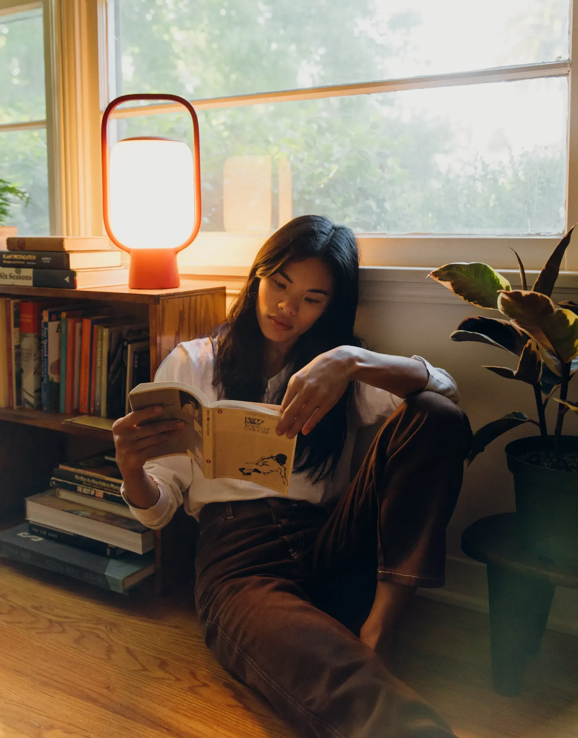 An Asian woman reading with the help of natural light from an open window and the light of an illuminated red Kero Table Light