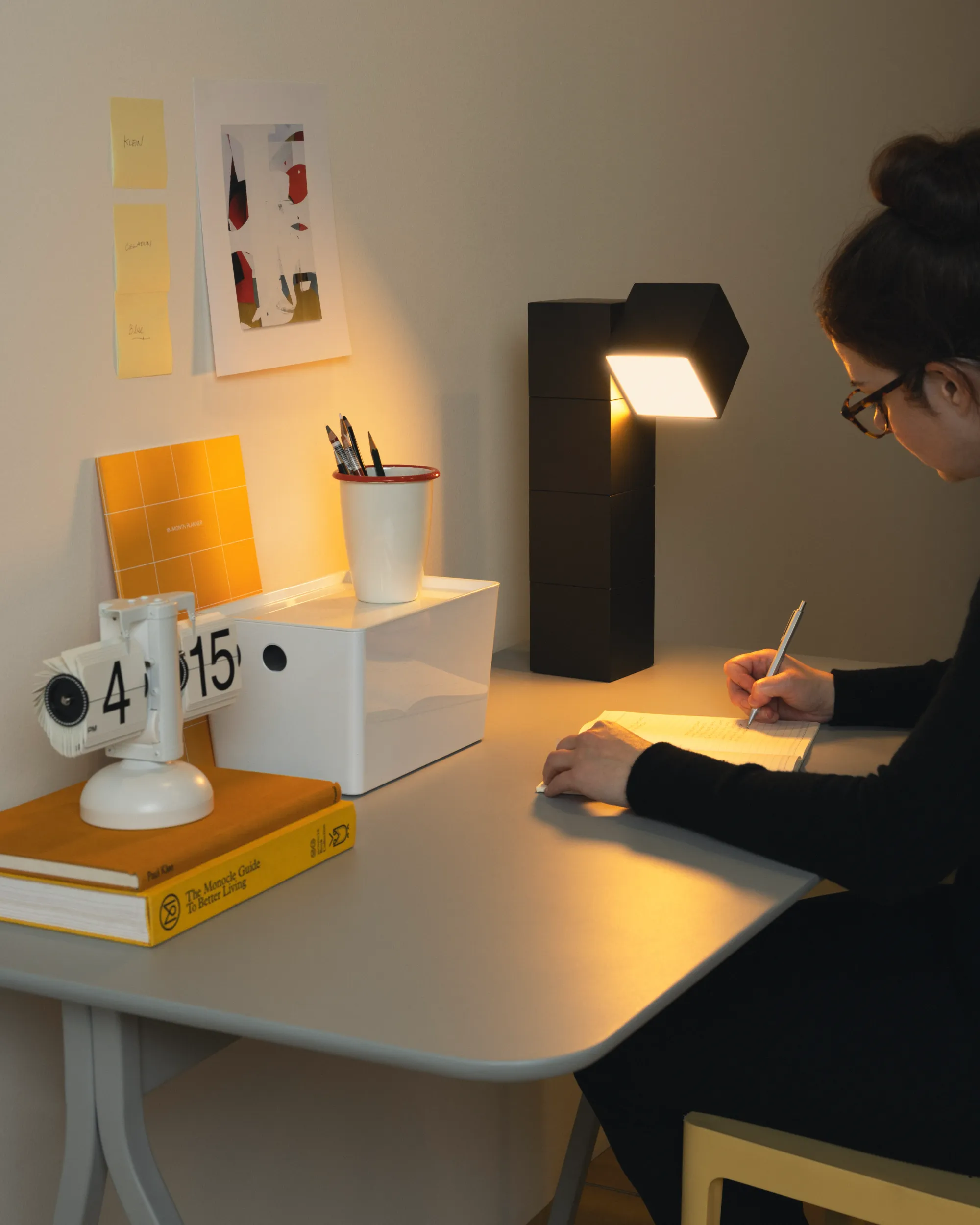 A woman is writing on her home office table which is illuminated by light from Gantri’s black Analog Task Light table lamp
