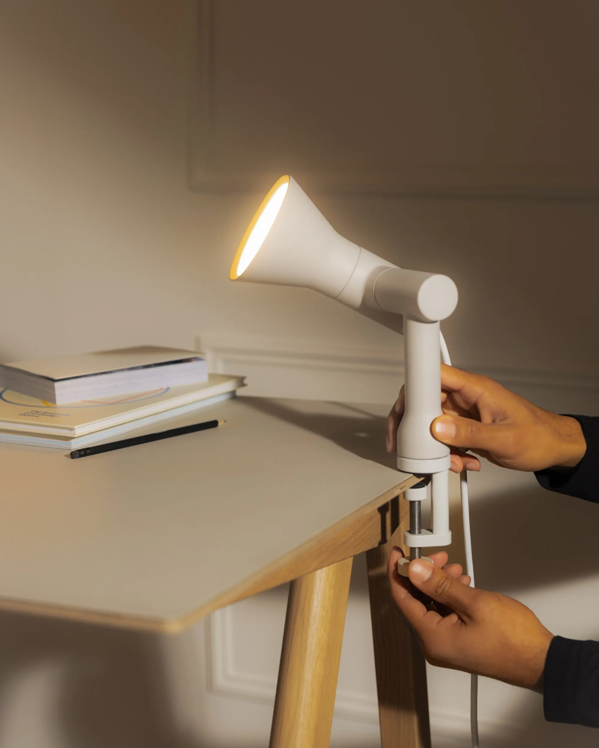 An illuminated Gallery Clamp Light by Gantri is being fastened on a home office table