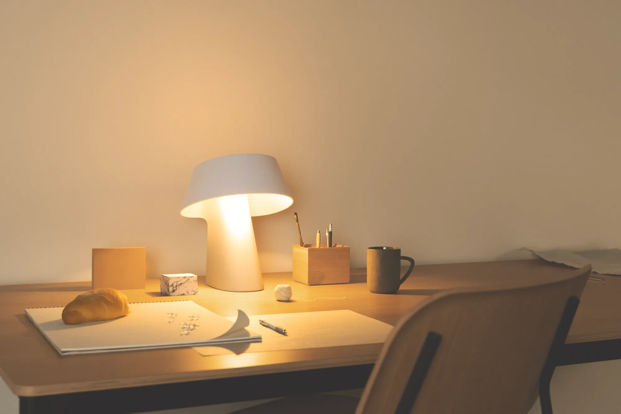 A desk lamp with a blank sketch pad, some drawing materials, a cup of coffee, and a piece of bread is illuminated with light by Gantri’s Fold table light