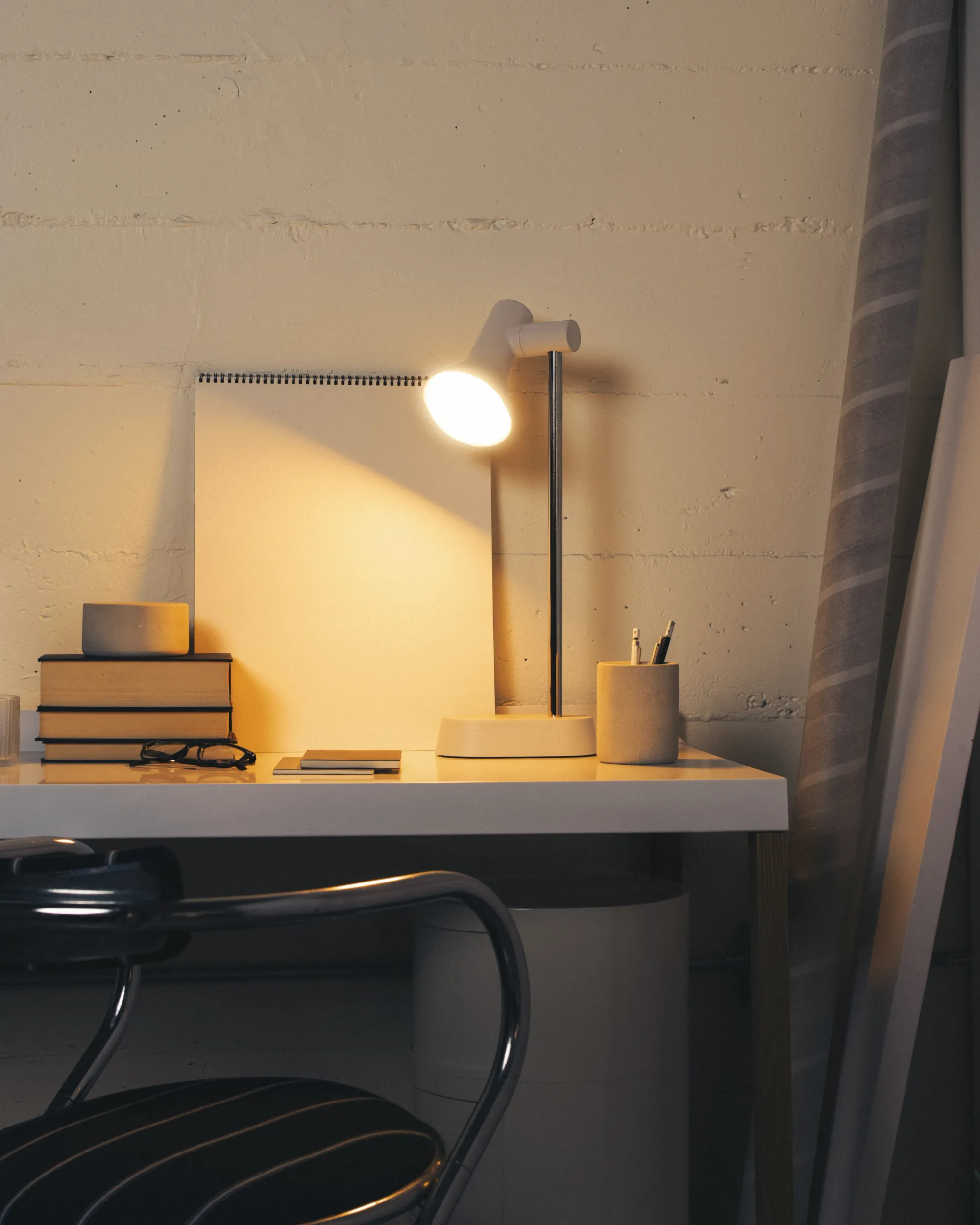 A small workspace filled with books, glasses, and writing materials are illuminated by light from an open Gantri Gallery Task Light.