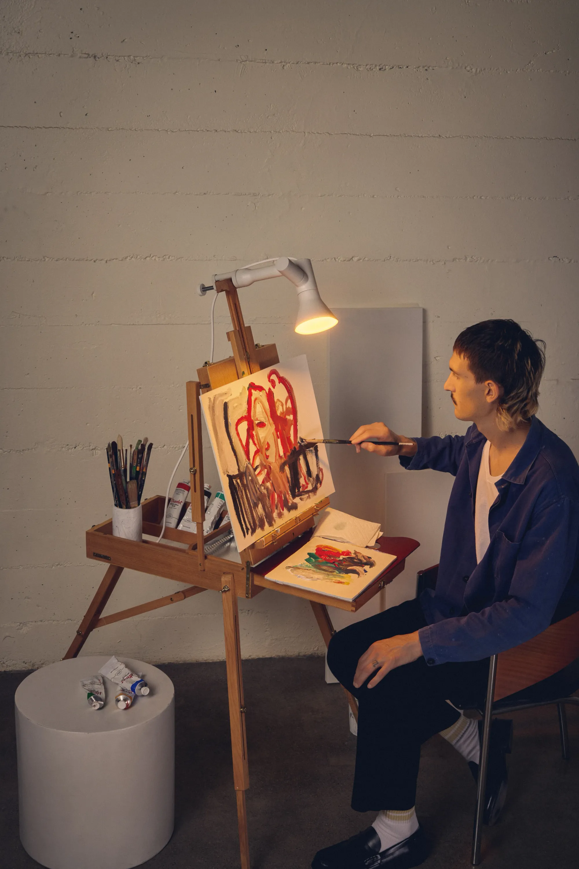 A man is painting using light from his white Gantri Gallery Clamp Light mounted on the top of his easel.