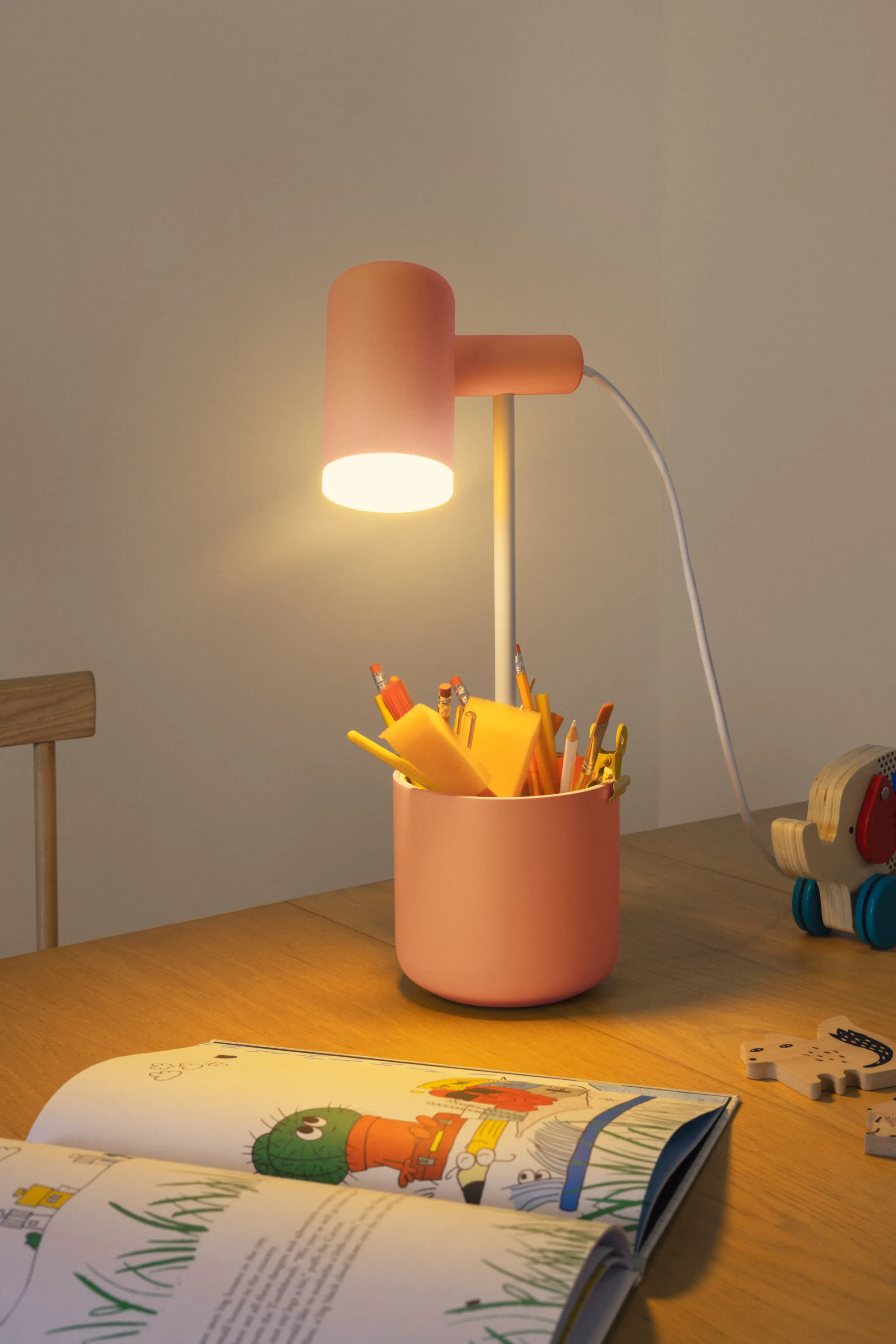 A Gantri Fieldtrip Table Light in blossom is filled with various writing materials and illuminates an open book,