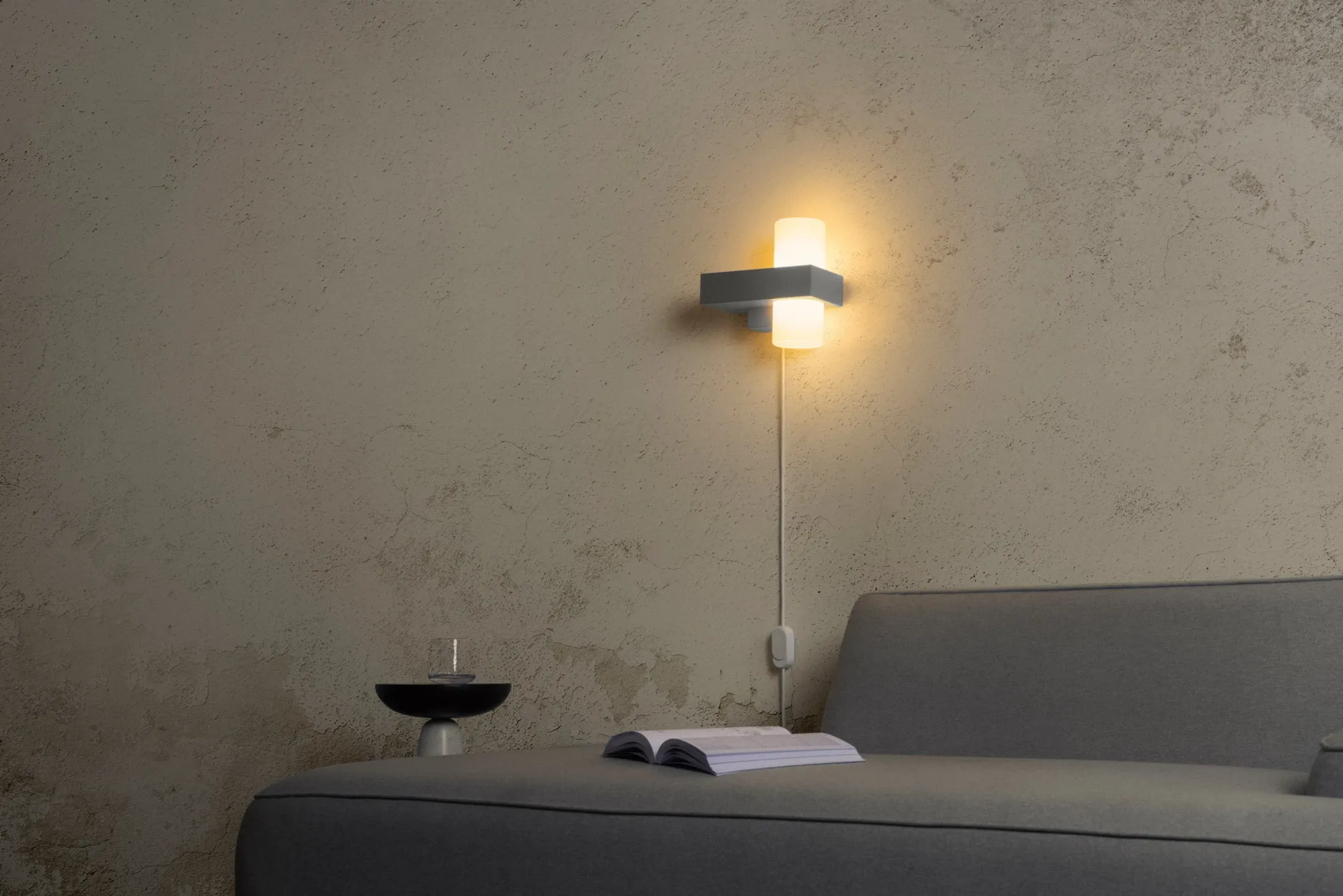 Gantri’s Figra Wall Light illuminates a gray couch where a book lies open