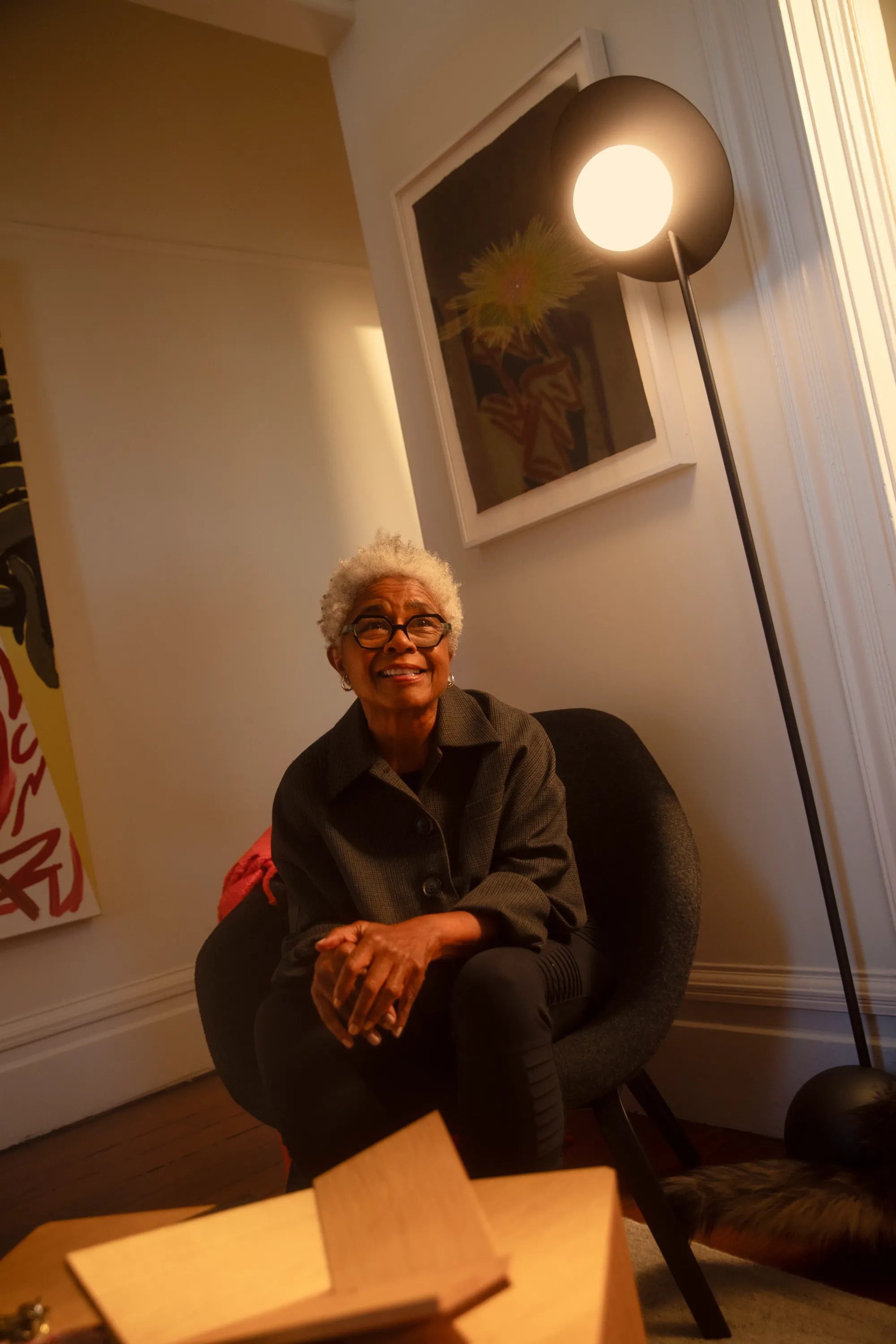 A Pavone floor light by Gantri illuminates the living room area of a middle-aged African American woman staring into the distance