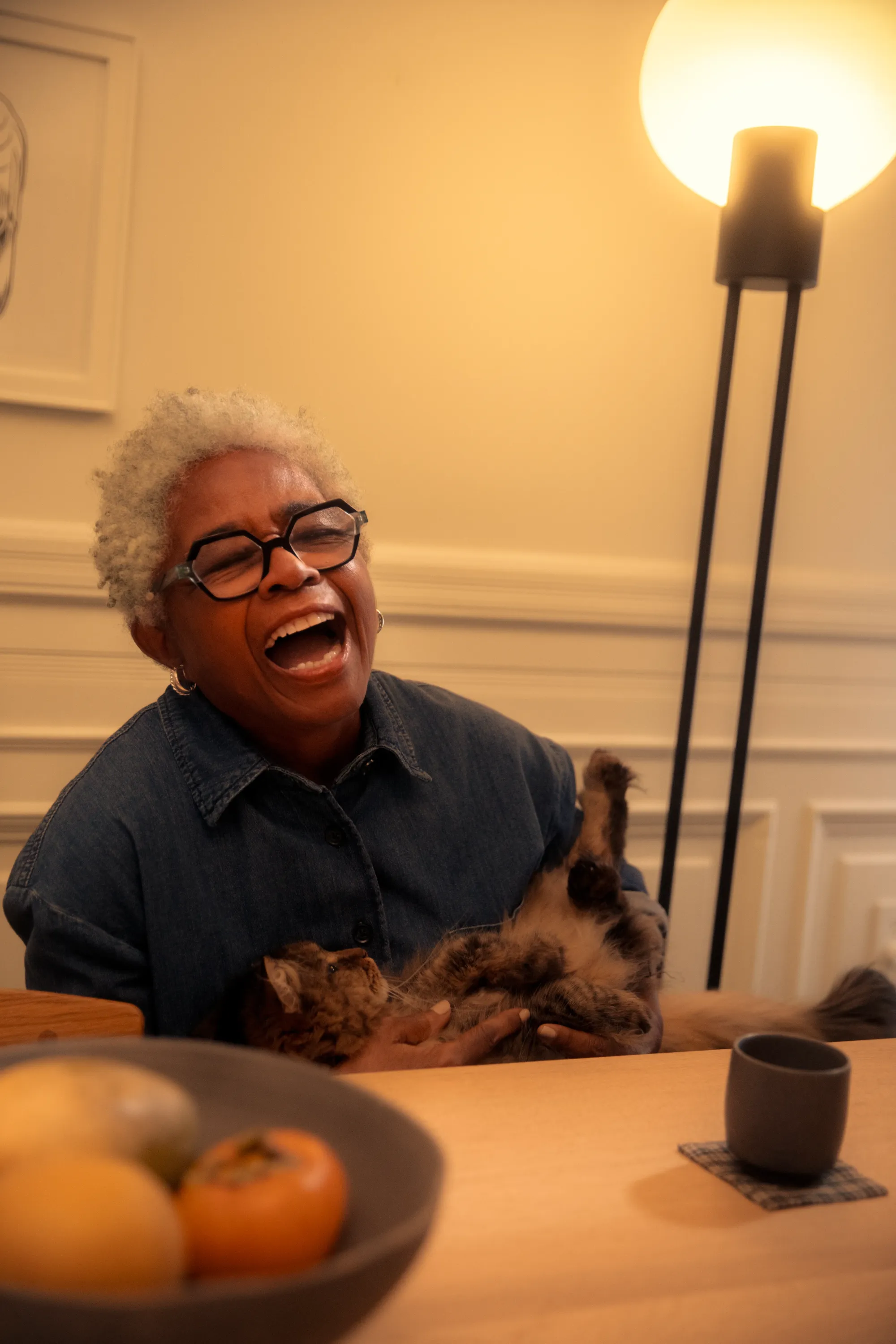 A middle-aged woman is laughing while holding her pet cat. She is illuminated by light from Gantri’s Pavone floor light. 