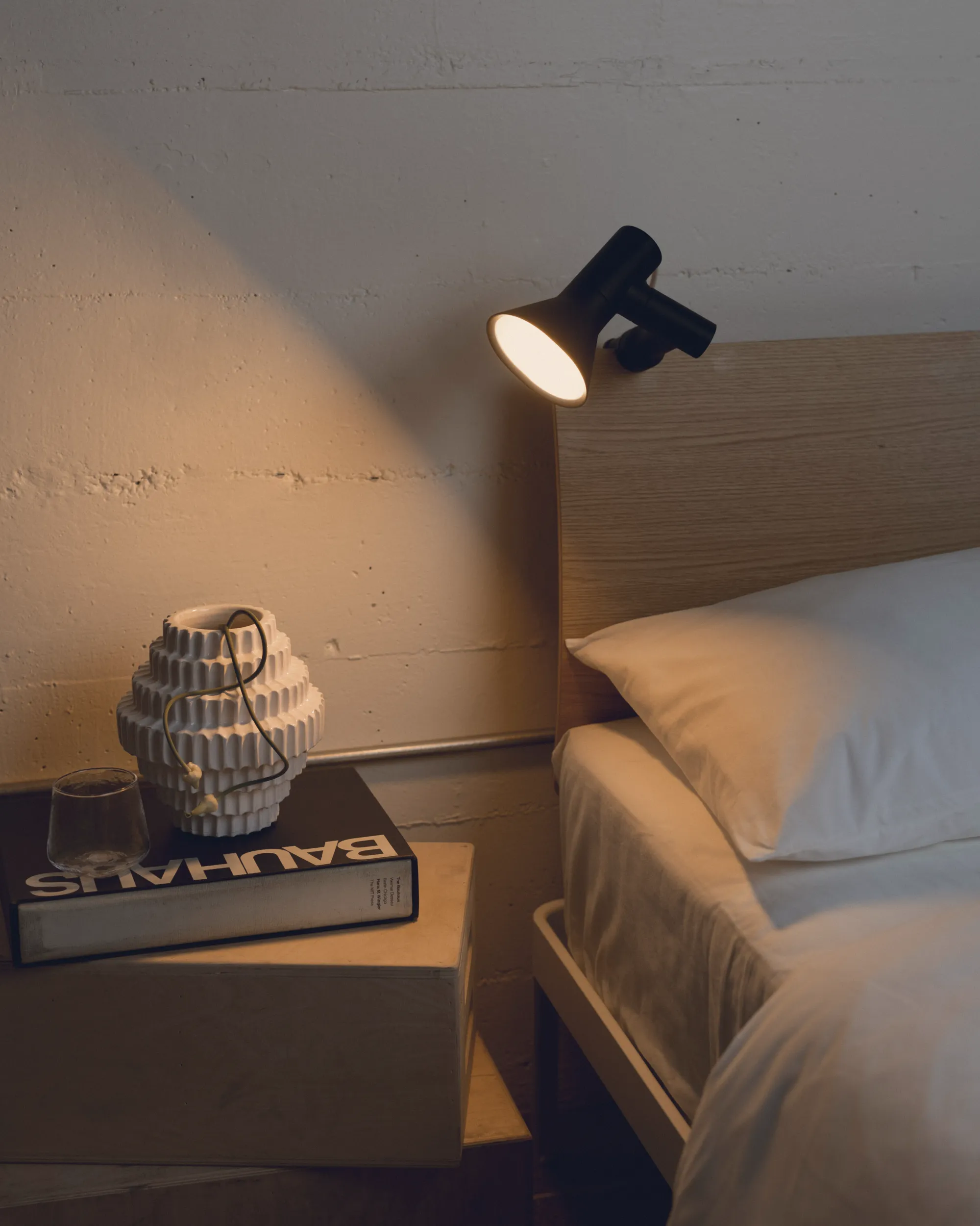 A bedside area with some books  is illuminated by a Gantri Clamp Light