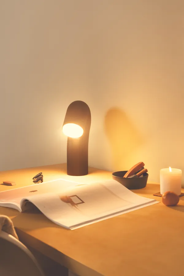 Gantri’s Smoothy table light illuminates an open book on a small wooden table. A small scented candle is also on the table.