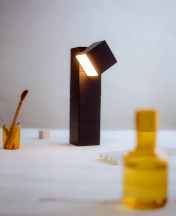 A lit Gantri Analog Task Light illuminates a table where a paintbrush can be seen hanging from a cup